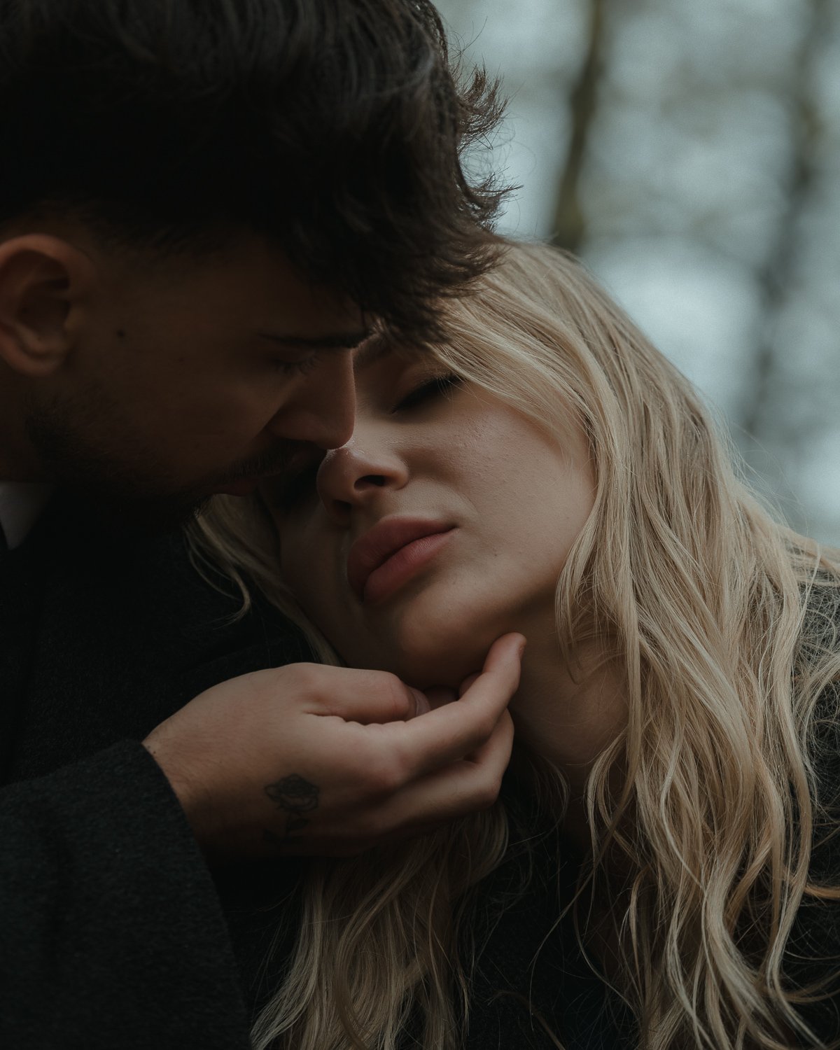 A close-up of a man and a woman in an intimate embrace outdoors, with the man's hand gently touching the woman's chin.