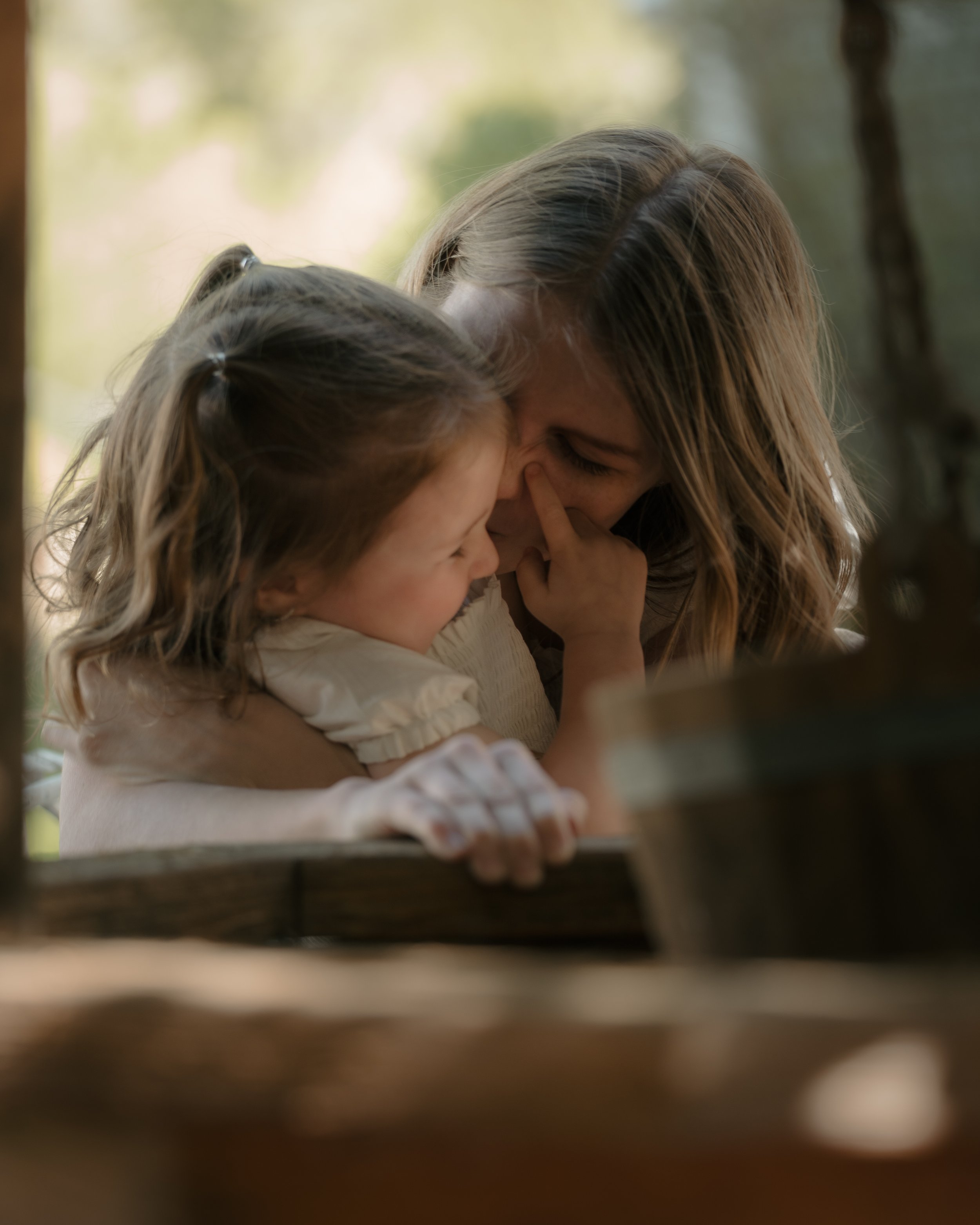 A woman and a young girl sharing a tender moment outdoors, with the woman gently touching the girl's face and both smiling.
