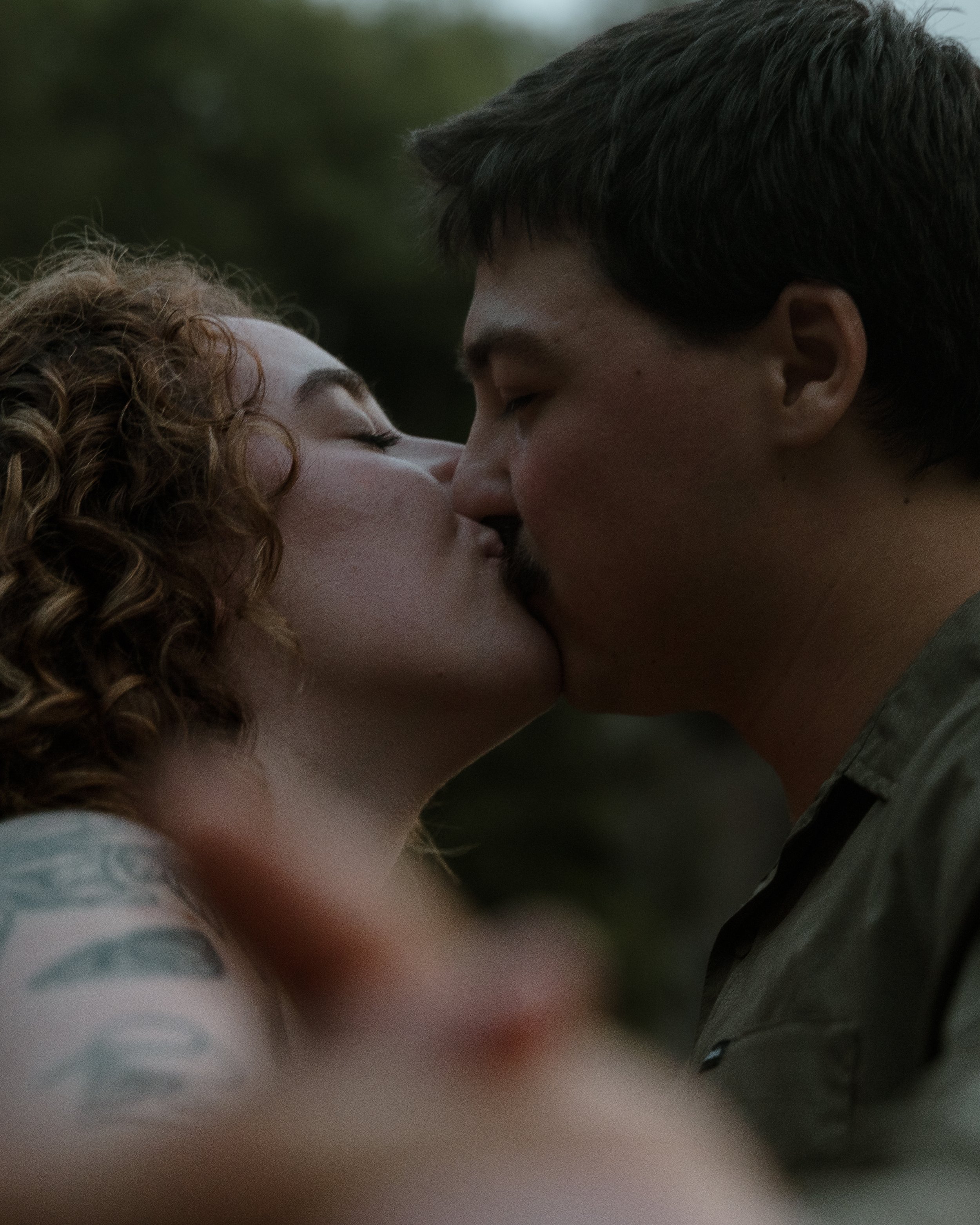 A man and woman are kissing outdoors with their eyes closed.