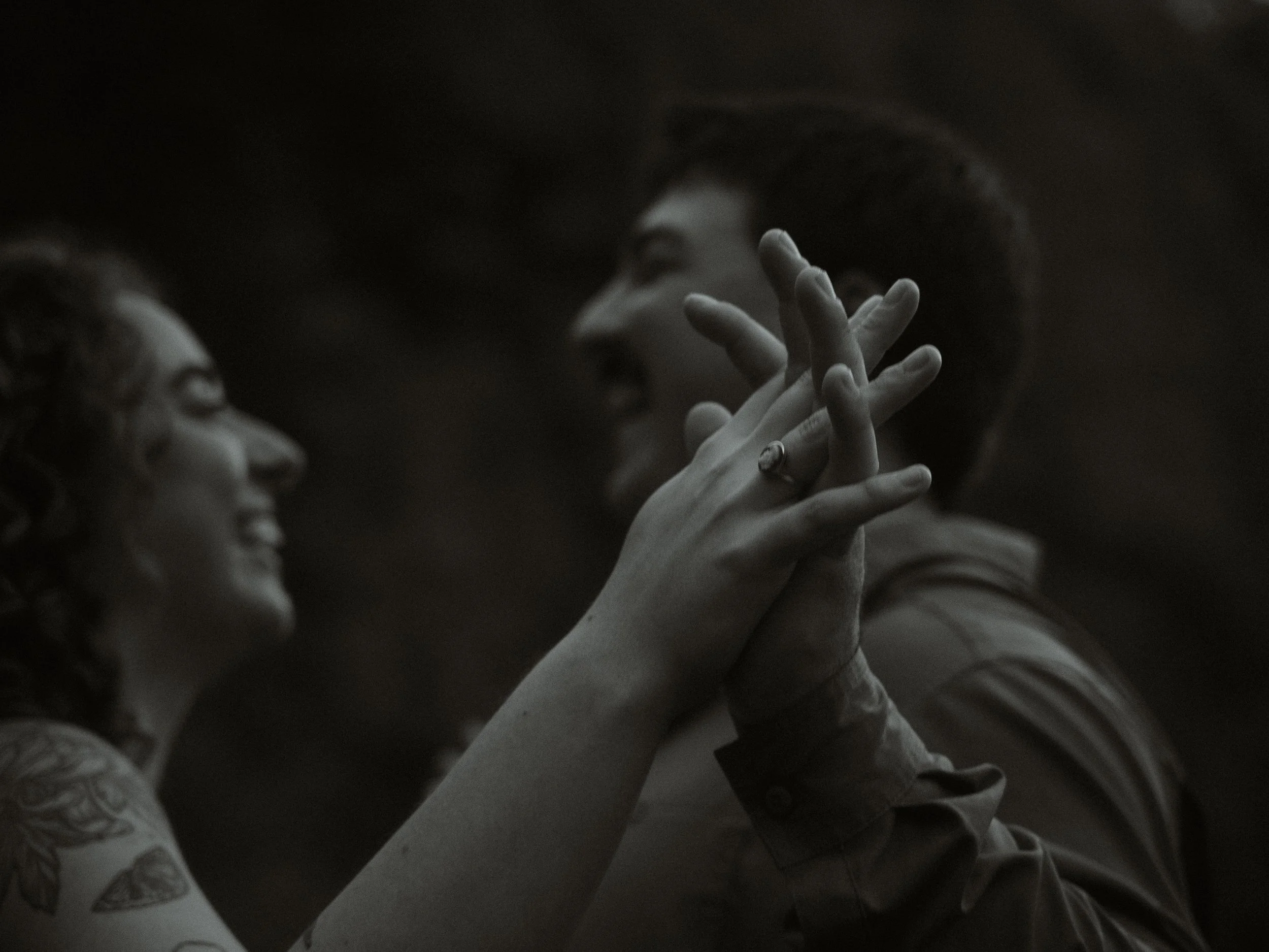 Close-up of three people holding hands, showing their forearms and fingers intertwined, with one person wearing a ring on their finger.