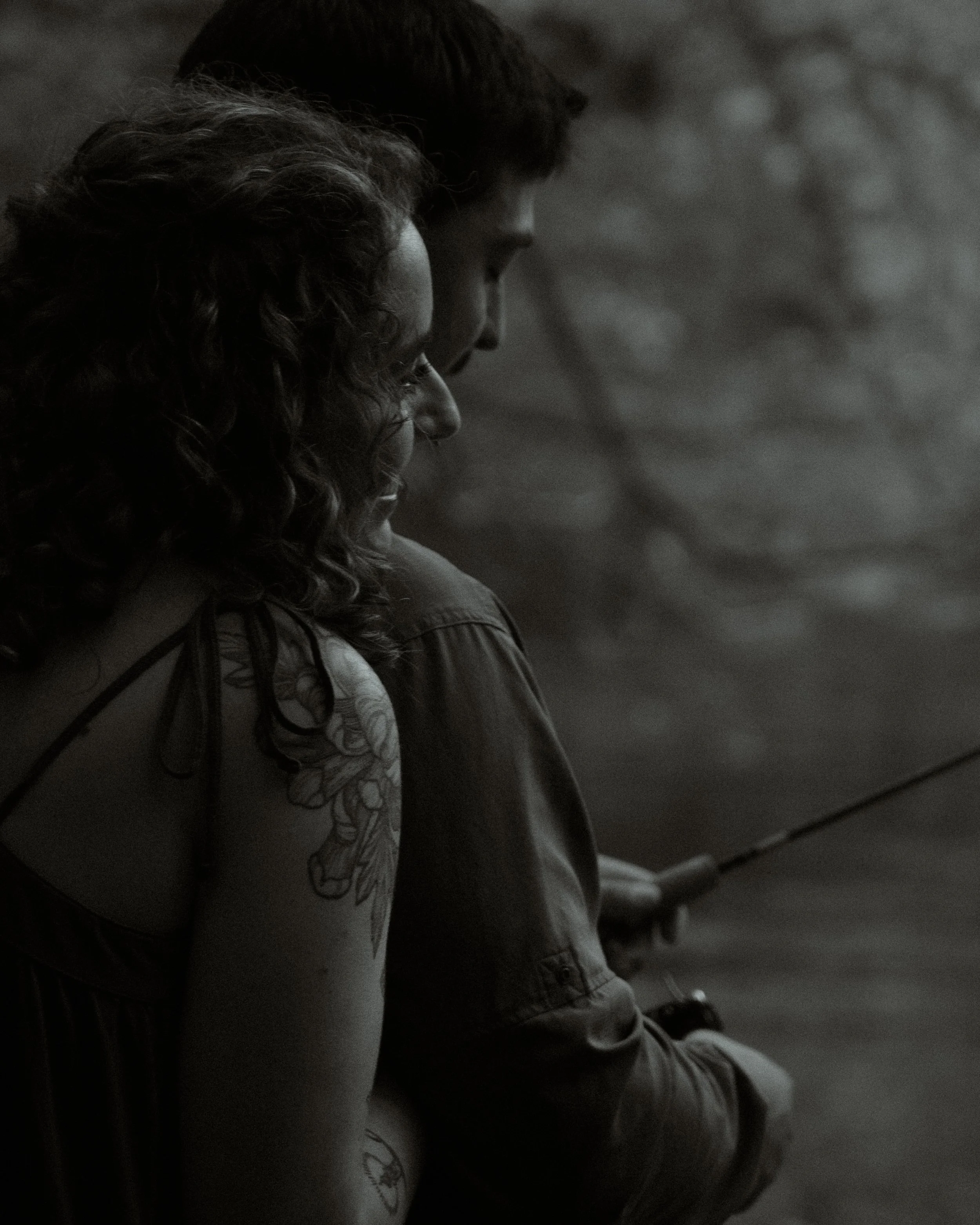 A black and white photo of a woman and a man fishing together, seen in profile, with the woman in the foreground.