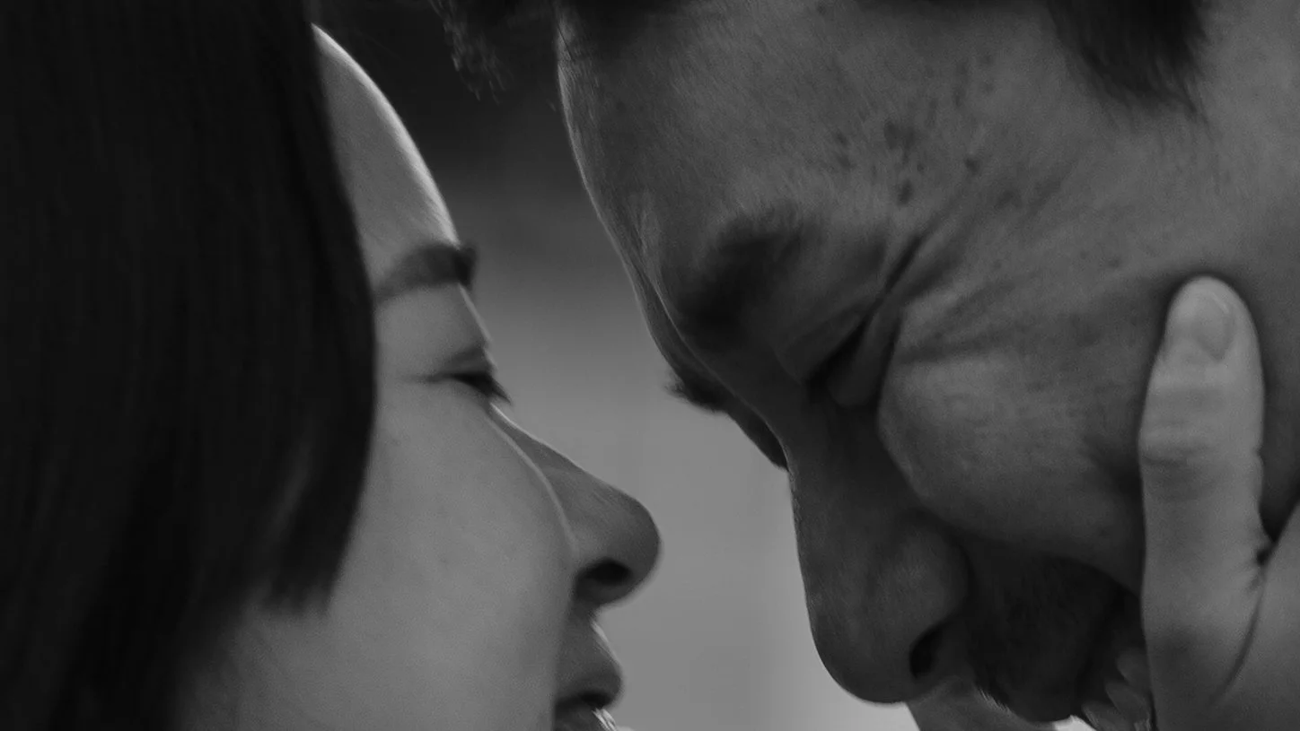 A close-up black and white photo of two people touching foreheads with their eyes closed, expressing intimacy.