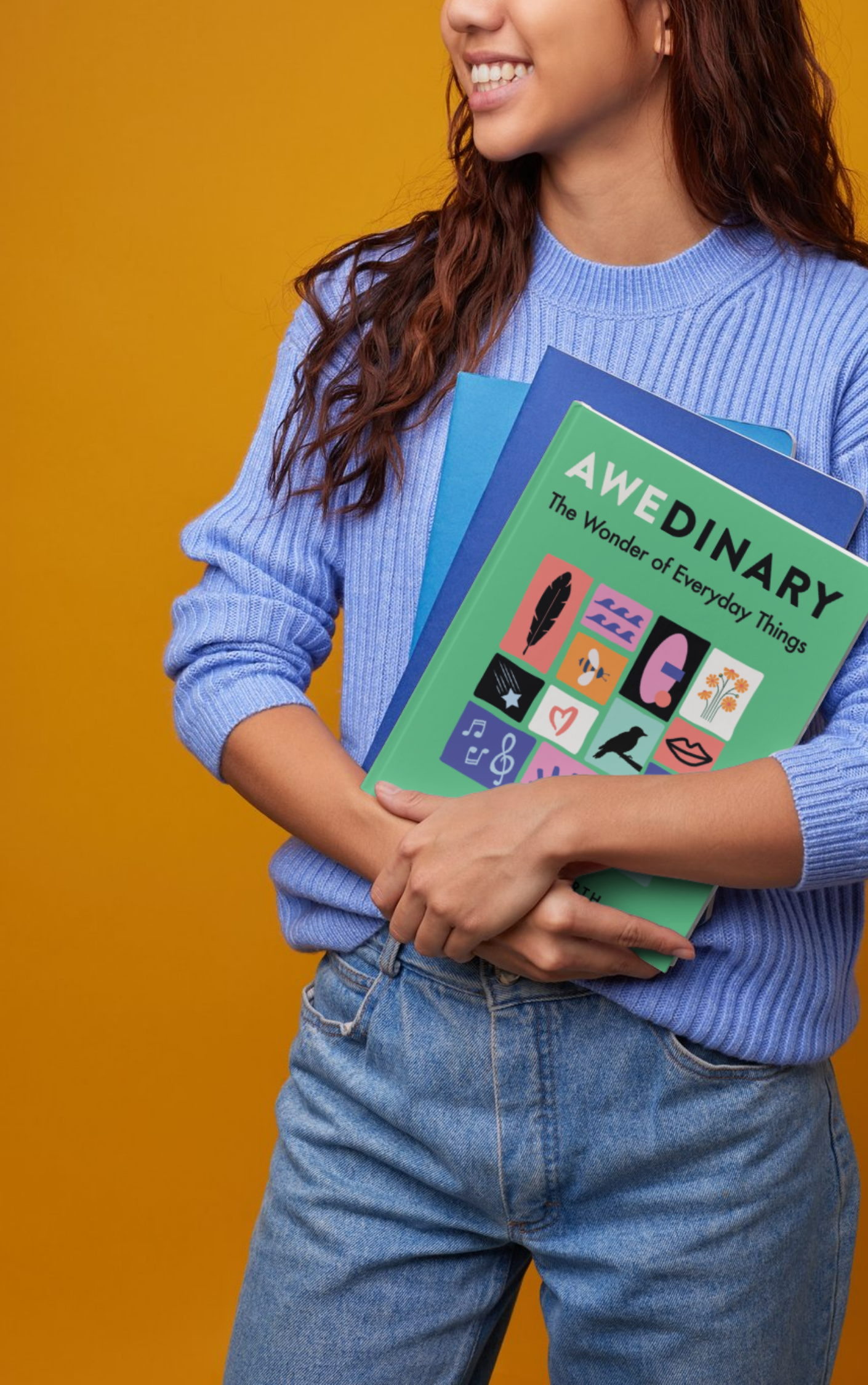 A woman wearing a light purple sweater holding a welcome book and folders, standing against a mustard yellow background.