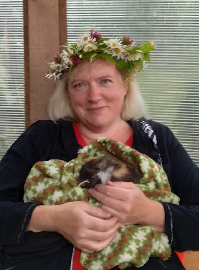 Frau mit Blumenkranz auf dem Kopf hält ein schlafendes Kätzchen, eingewickelt in eine weihnachtliche Decke.