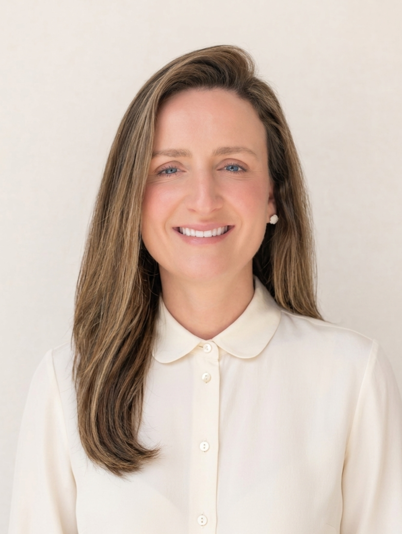 A woman with long, light brown hair and blue eyes wearing a white collared blouse, smiling against a plain light background.