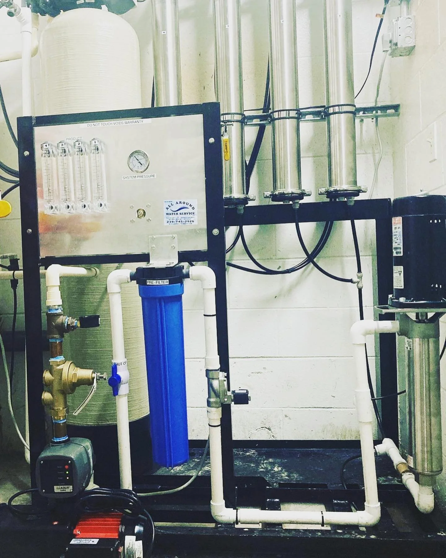 An industrial water filtration system with pipes, filters, and gauges, mounted on a wall in a utility room.