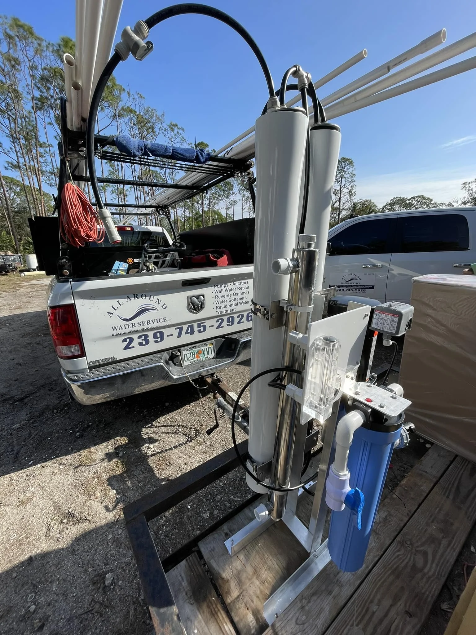 A water filtration system installed on a trailer, with pipes, filters, and other equipment, set outdoors on a gravel surface with trees in the background.
