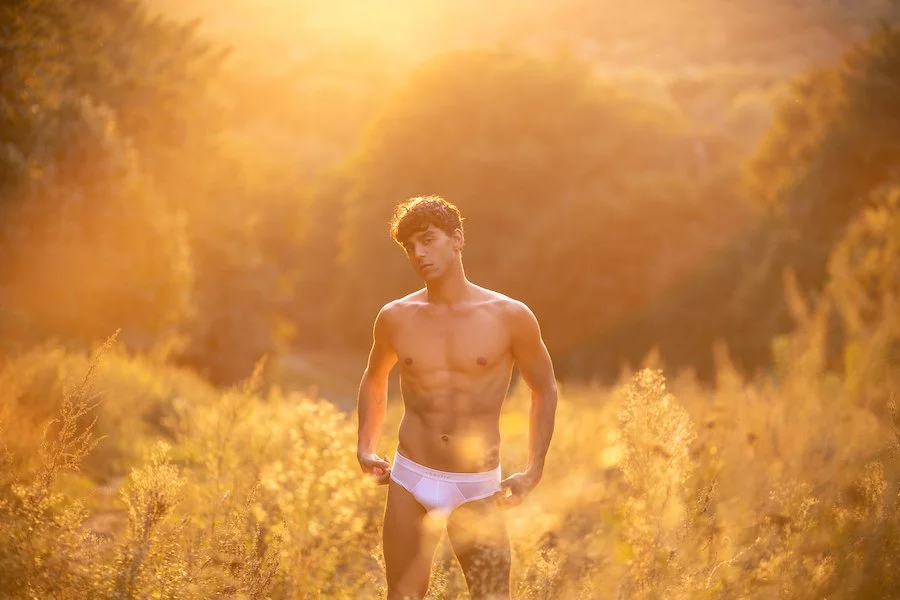 A young man in his underwear standing in a sunset in a field. Photo by @papagnimeca