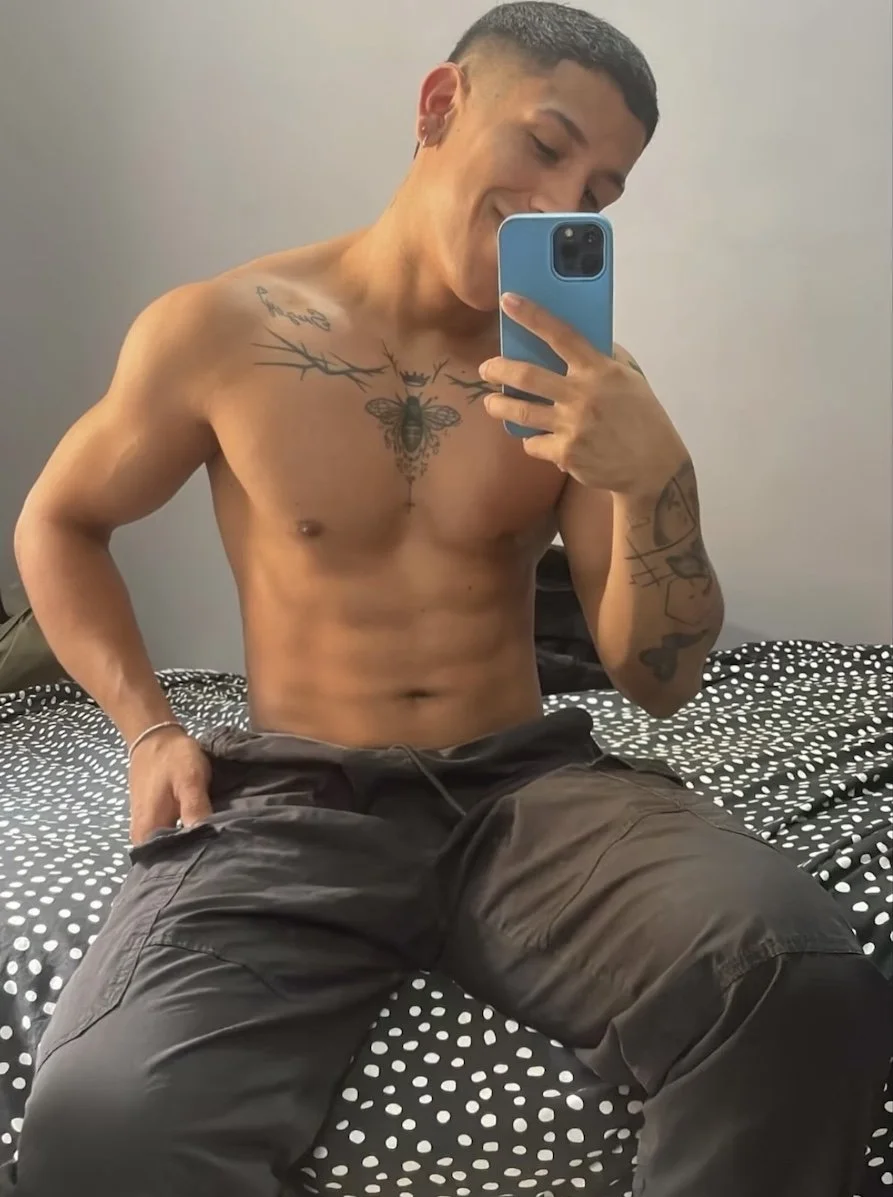 Jeferson sits shirtless on bed, taking a selfie