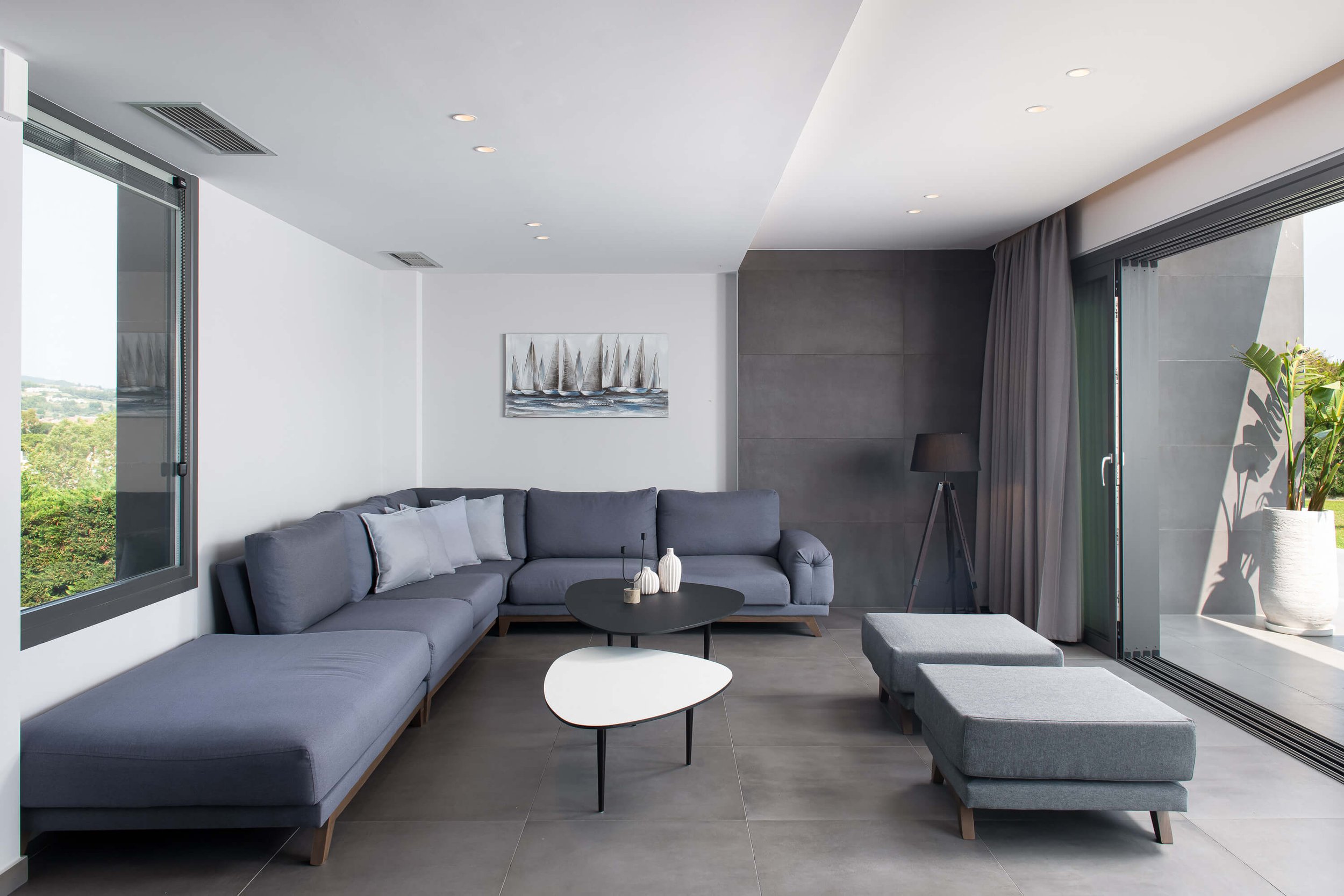 Modern open-plan living room of Antonio Villa Hanioti featuring grey sofa, ottomans, round coffee table and breathtaking sea horizon through floor-to-ceiling glass