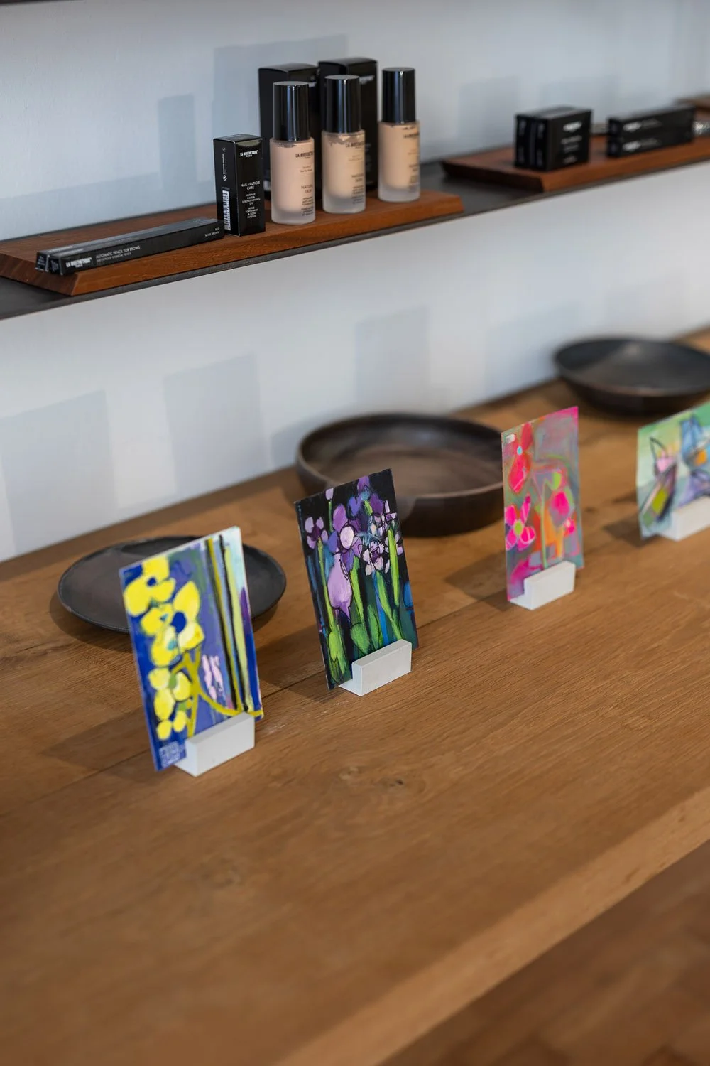 Kleine bunte Kunstwerke auf Holzständern, ausgestellt auf einem Holztisch.