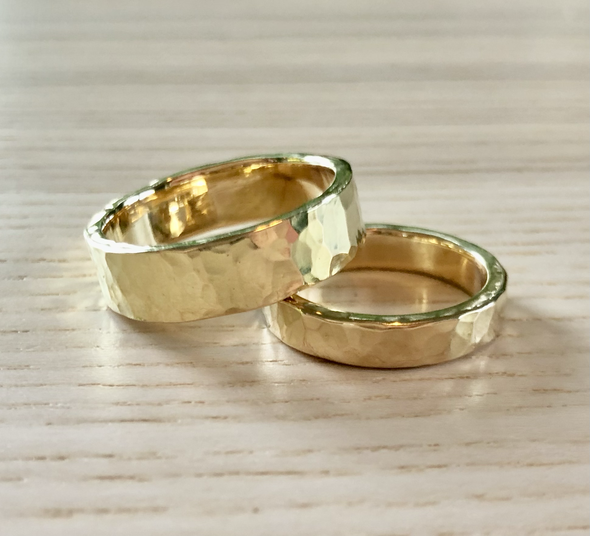 Two gold wedding bands with hammered texture, placed on a light wooden surface.