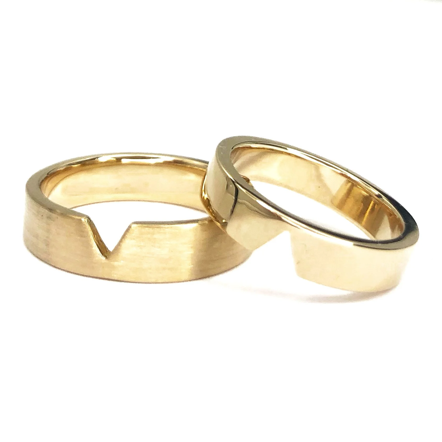 Two gold wedding bands with one featuring a V-shaped notch, placed against a white background.