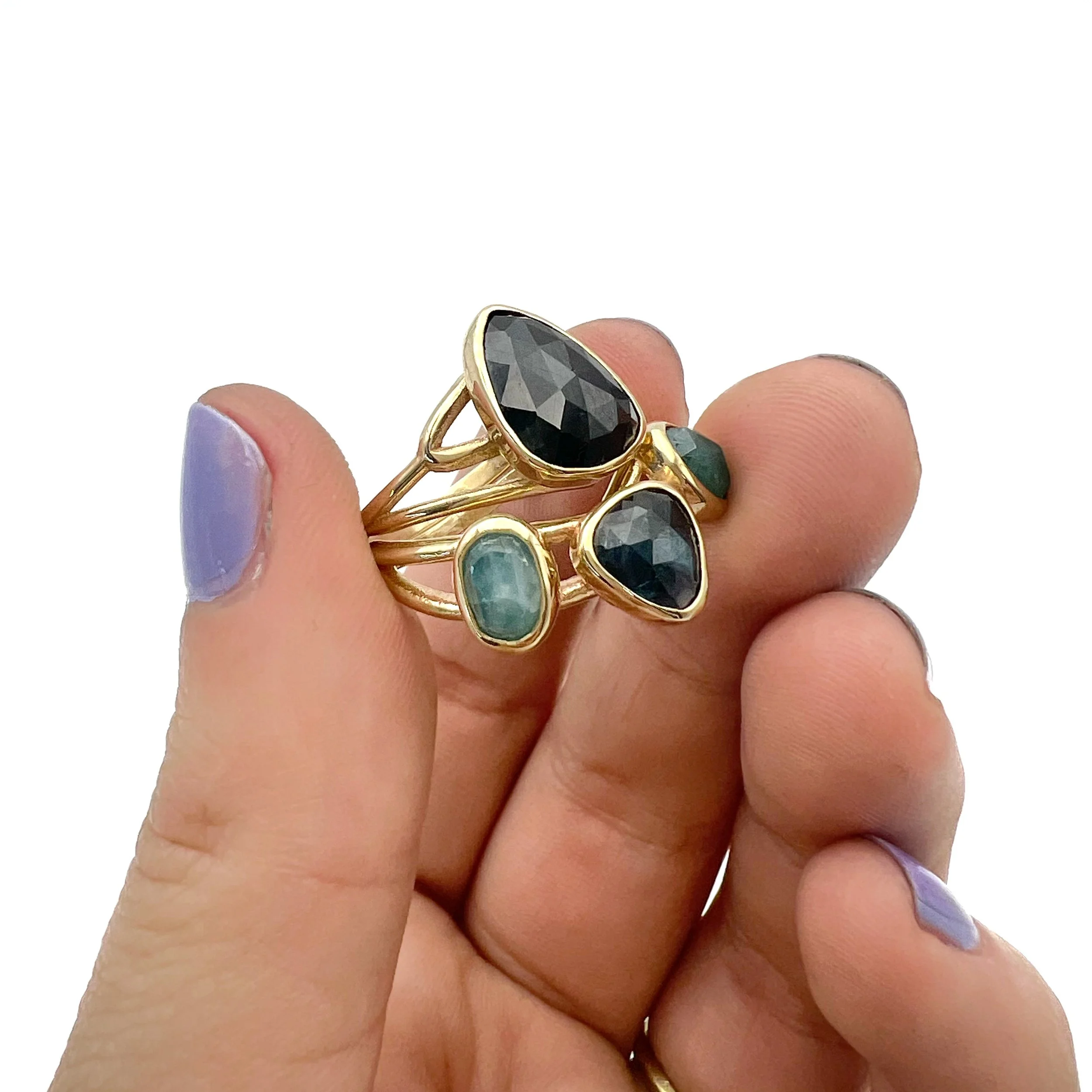 Hand holding multiple gold rings with black and green gemstones, white background