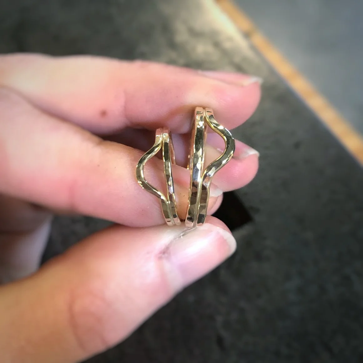 A hand holding two gold rings with wavy designs.