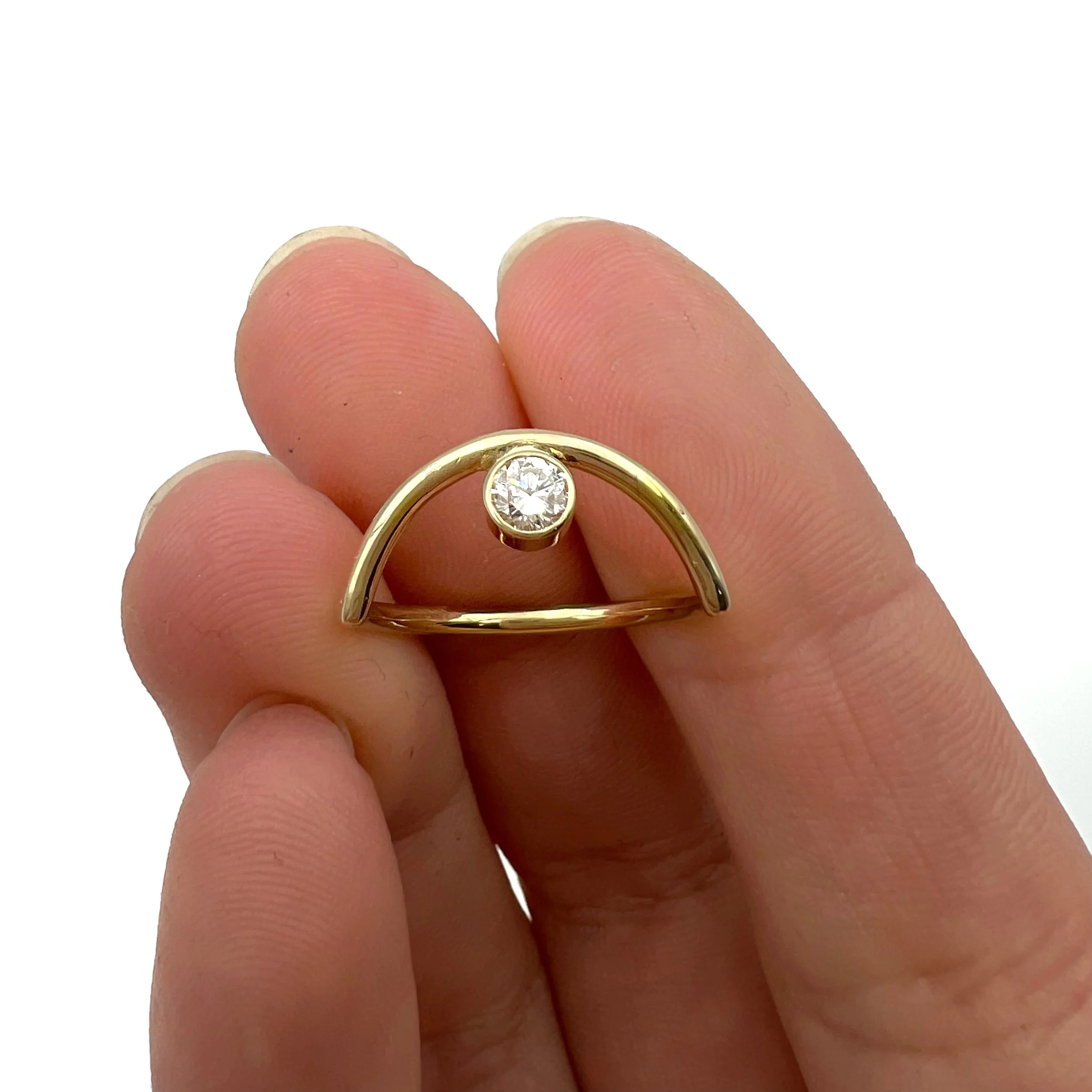 Hand holding a gold ring with a semi-circle design and a single small diamond in the center against a white background.