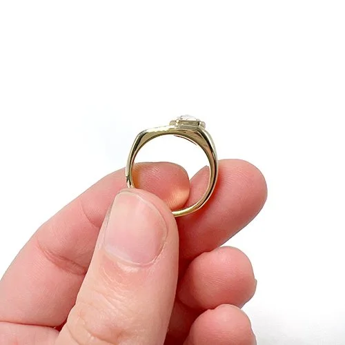 A person holding a gold ring with a small gemstone set in a prong setting.