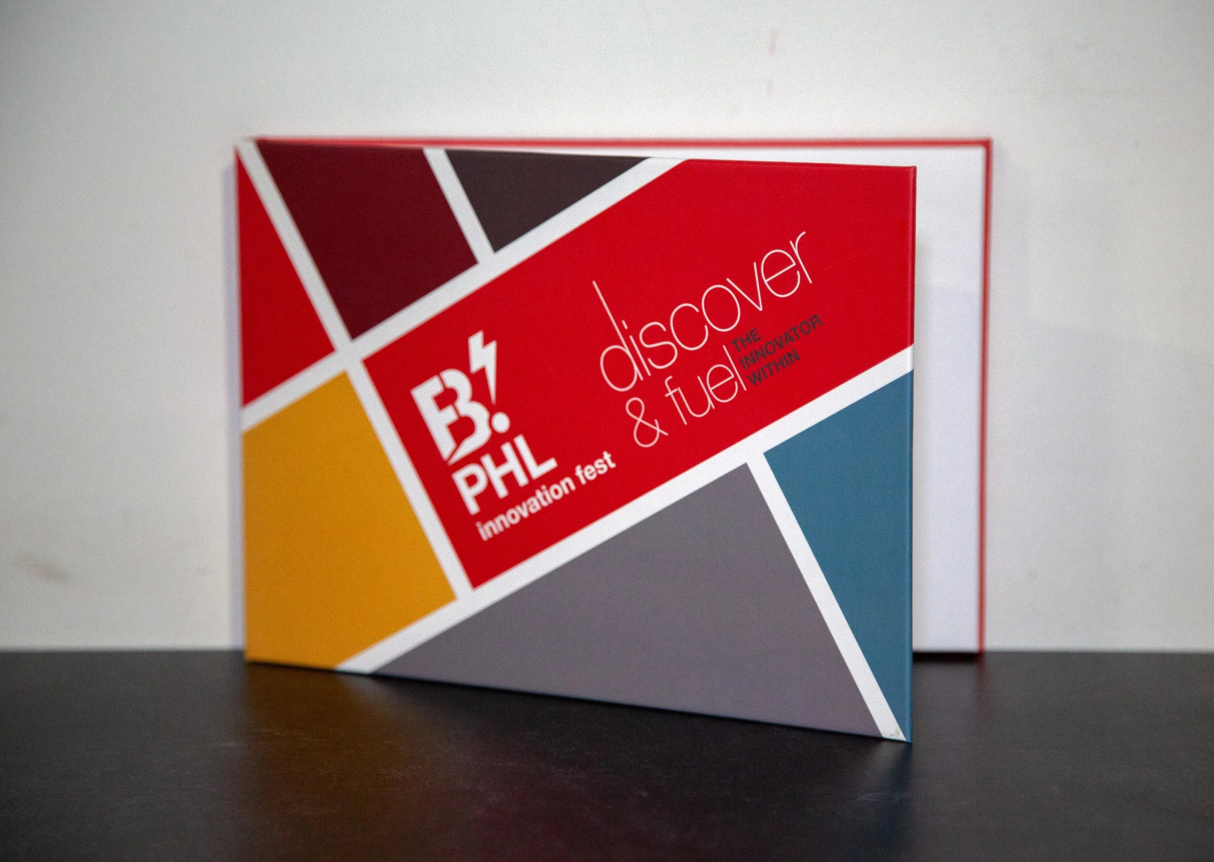 Colorful brochure titled 'B! PHIL innovation test discover & fuel the innovator within' placed on a dark table against a white wall.