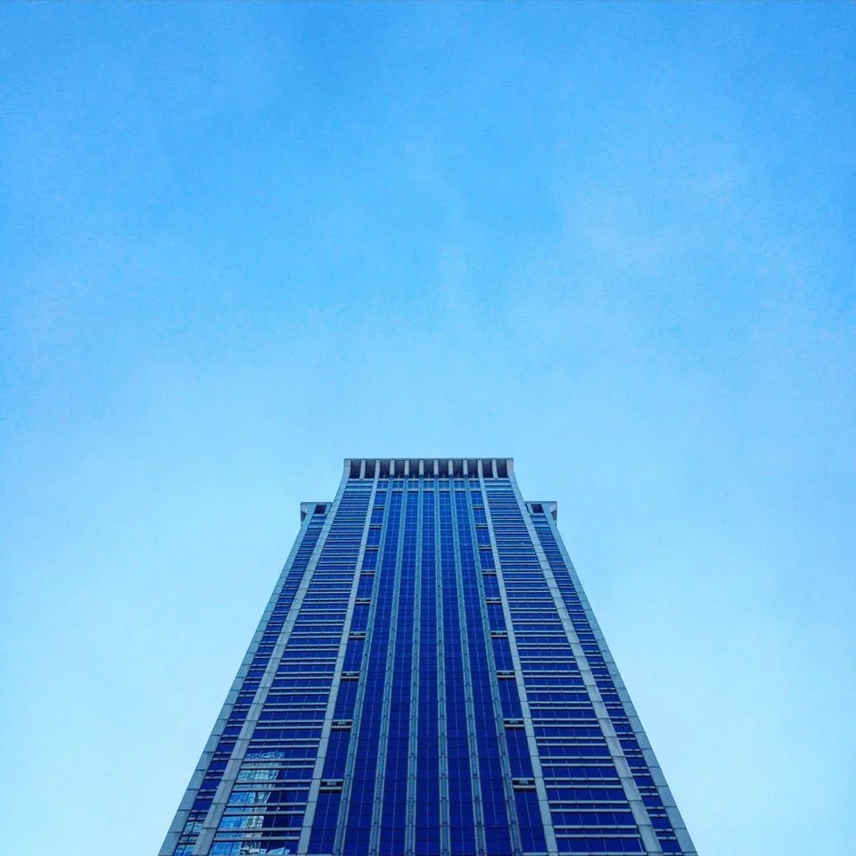 Look up at a tall blue skyscraper against a clear blue sky.