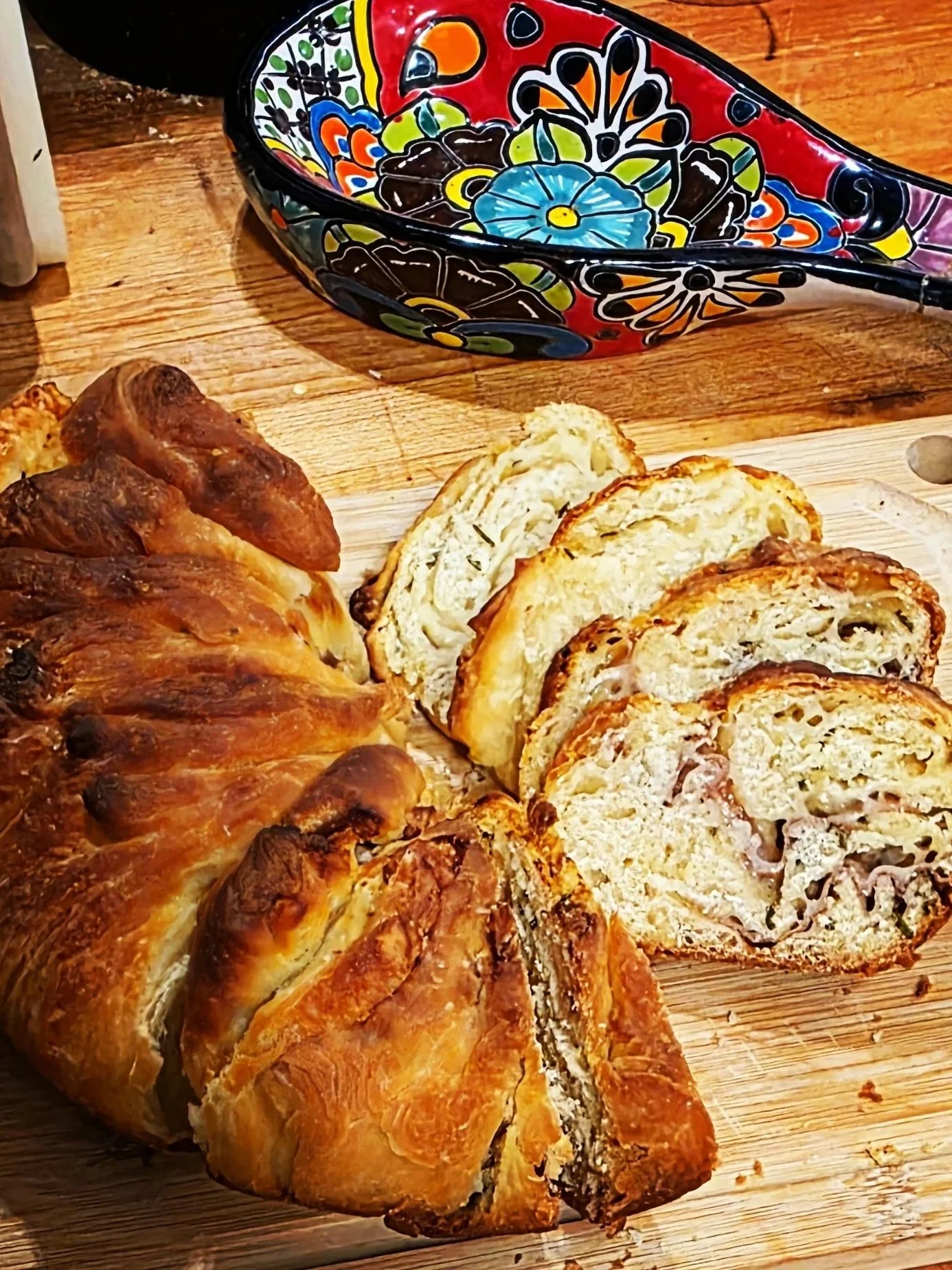 Sliced stuffed savory bread on a wooden cutting board with a colorful decorative bowl in the background