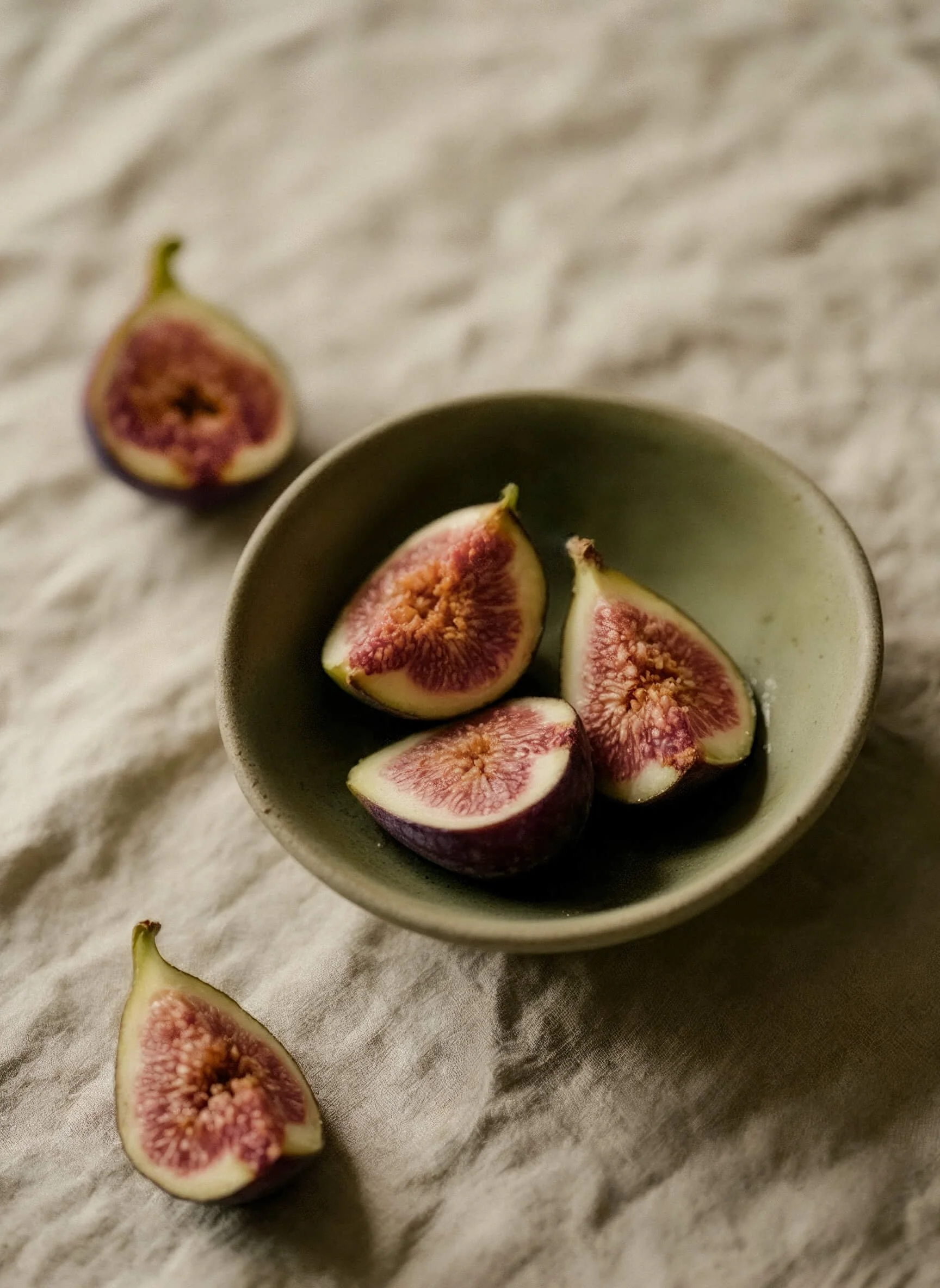 A small bowl with four sliced figs and two additional figs on a soft, light-colored fabric surface at Off Beet Holistic FDN in Birmingham, AL.