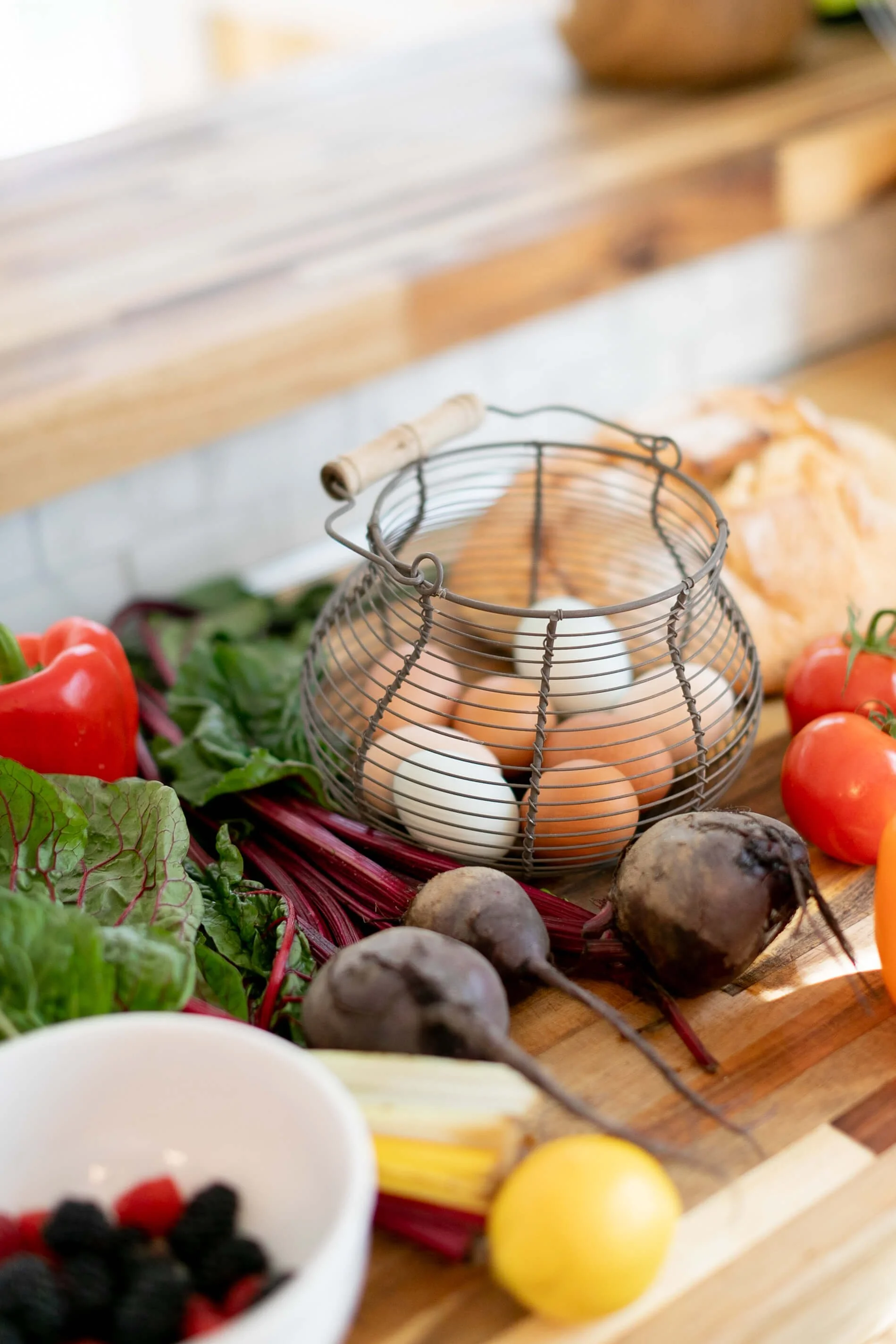 Fresh farm eggs in a wire basket surrounded by vegetables including beetroot, tomatoes, and leafy greens on a wooden surface at Off Beet Holistic FDN nutrition practice.