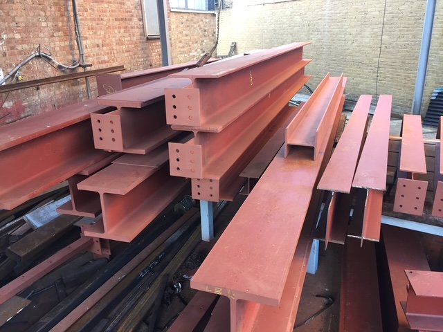 Red-primed steel beams with end plates stacked for delivery.
