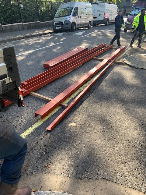 Red-primed structural steel beams laid out beside a construction site for installation.