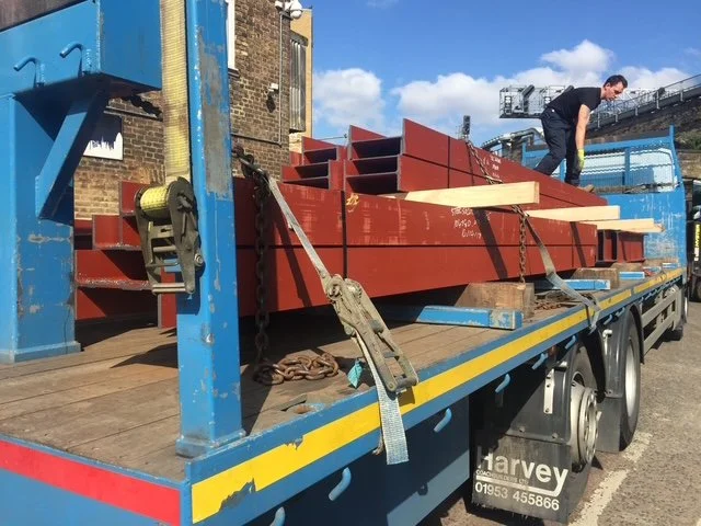 Steel beams being loaded onto a flatbed lorry using workshop lifting equipment.