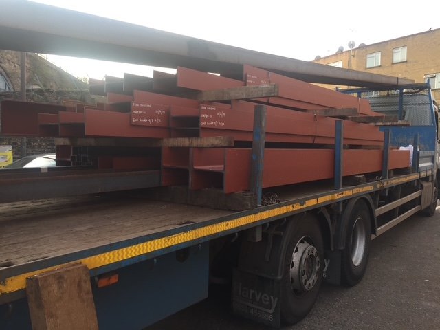 Red-primed structural steelwork secured on a flatbed delivery lorry.