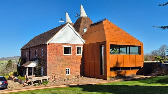 Wide garden view of a weathering-steel extension joined to a brick oast house.
