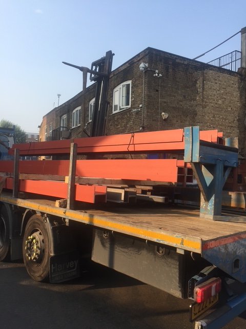 Structural steel beams on a delivery lorry outside a building under construction.