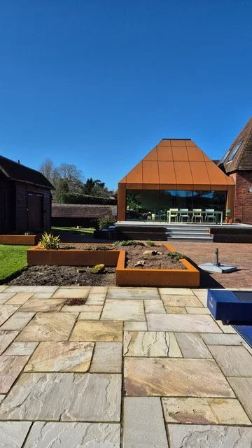 Garden terrace and raised planters leading towards a Corten steel-clad extension.