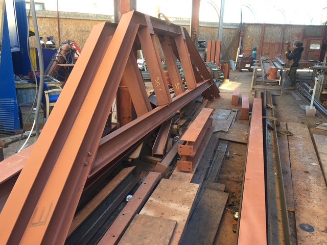 Fabricated red-primed steel roof frames stored in the workshop.