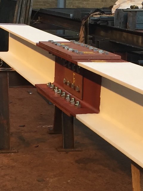Bolted splice connection joining two structural steel beam sections on workshop supports.