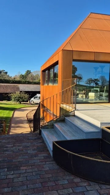 Corten steel-clad extension with full-height glazing opening onto a garden terrace.