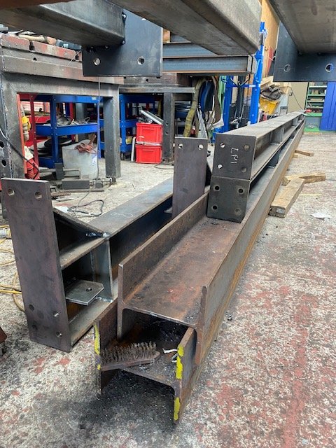 Fabricated structural steel beams with welded end plates in the workshop.