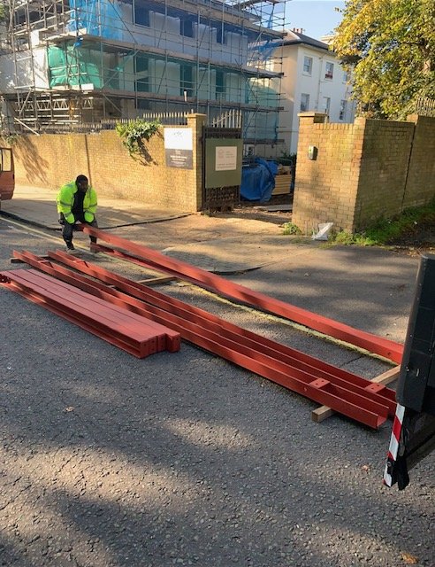 Builders beams with red protective primer being prepared for delivery into a building site.