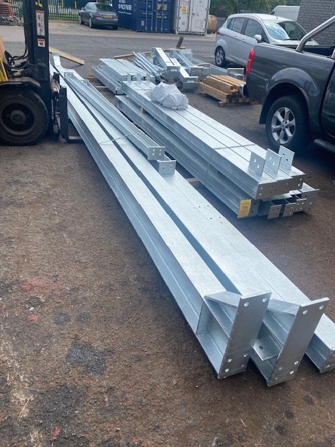 Long galvanised steel sections with end plates loaded on lifting forks outside the workshop.