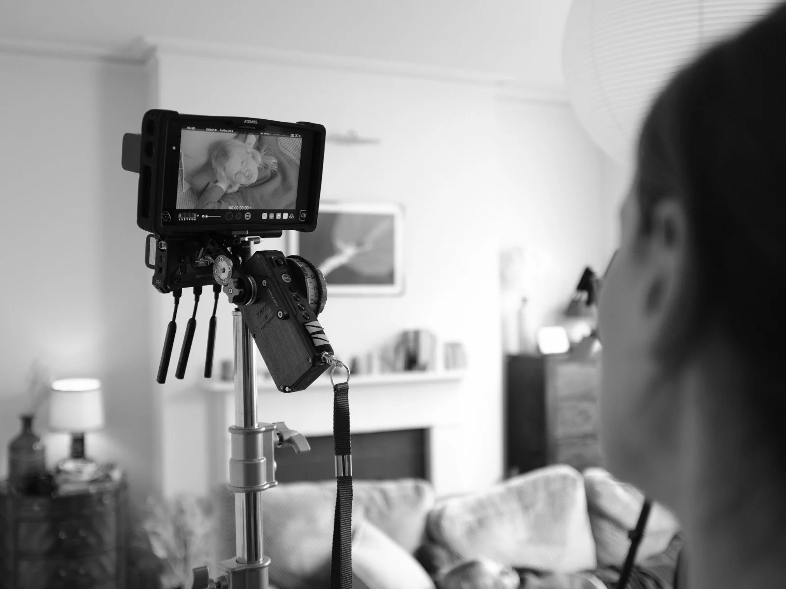 A person filming a woman lying on a bed with a professional video camera in a cozy living room.