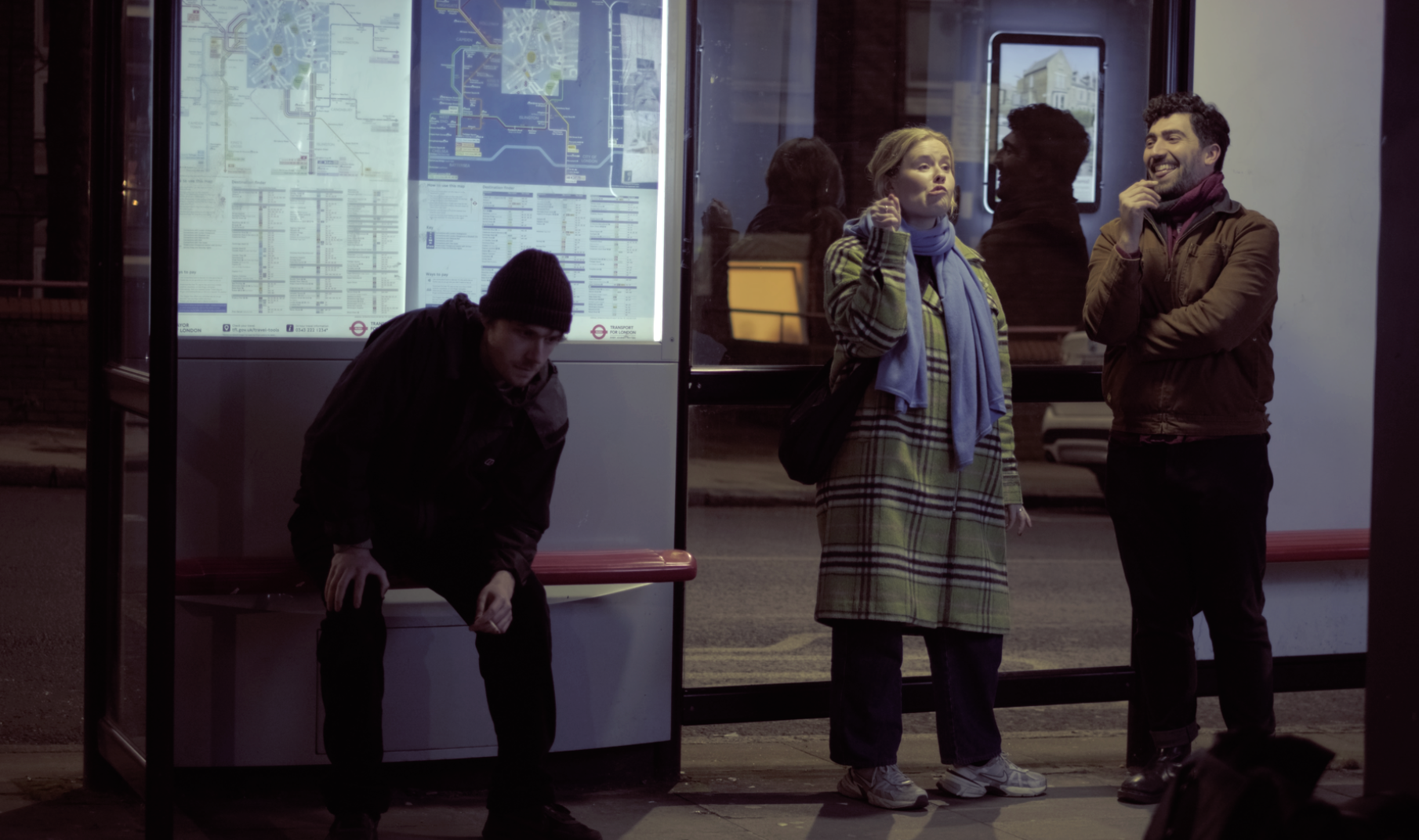 People waiting at a bus stop, one person is sitting, including women and men dressed warmly, with a city map in the background