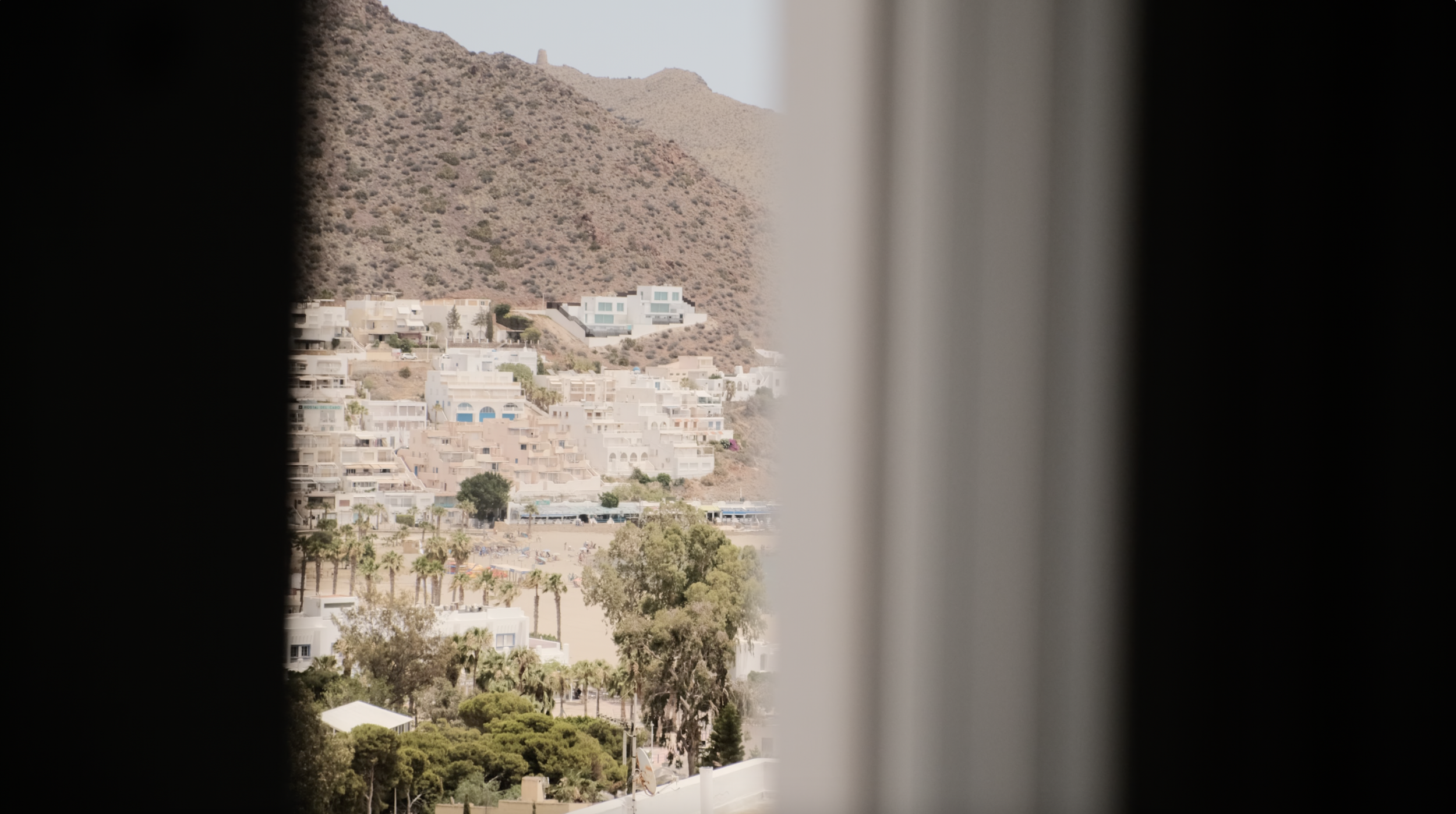 View of a hillside town through a window, with buildings and trees visible.