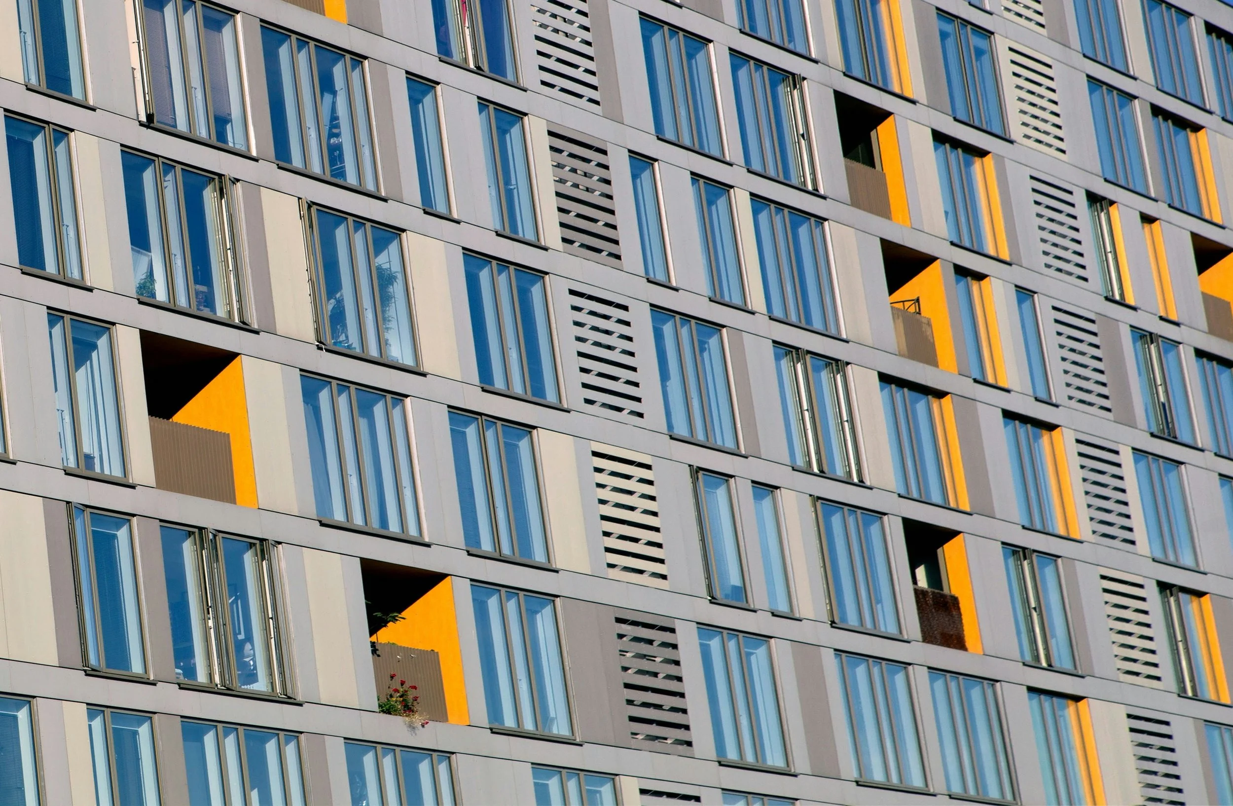 Close-up of a modern building facade with multiple windows and balconies, accented with yellow and gray panels.