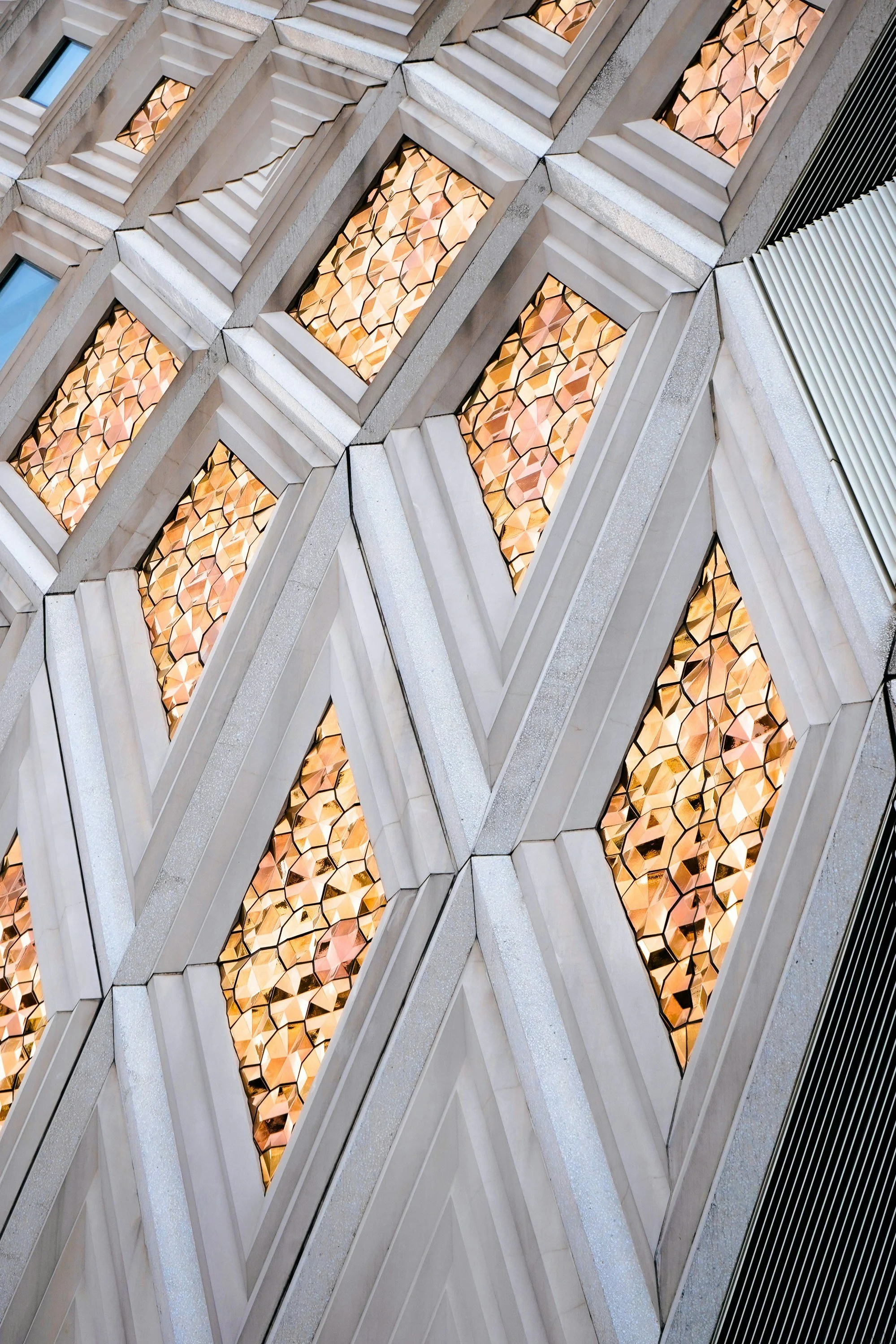Close-up of a modern building facade with geometric glass windows and illuminated decorative panels inside, creating a repeating pattern.