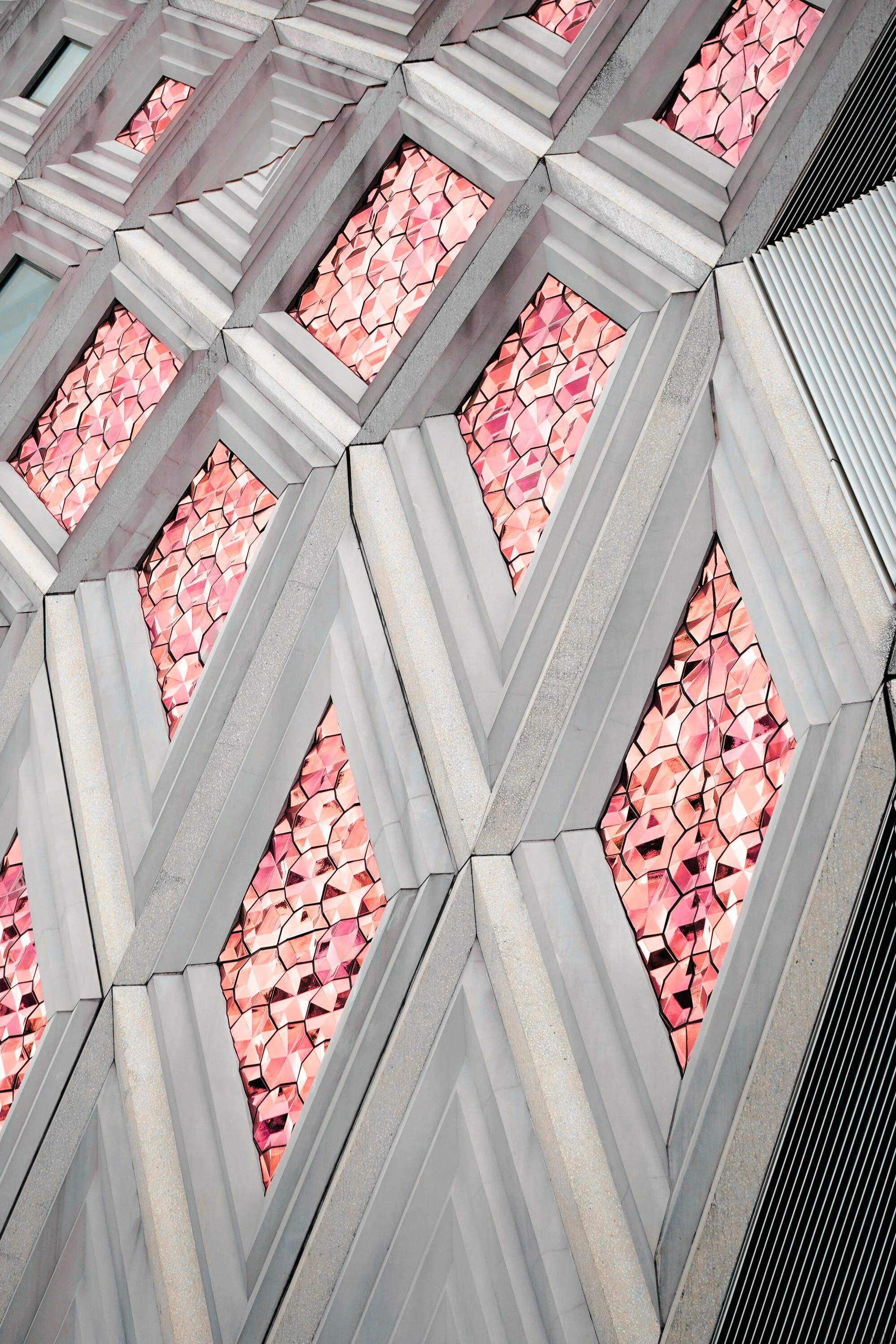 Close-up of a modern building facade with diamond-shaped pink stained-glass windows framed by gray concrete edges.