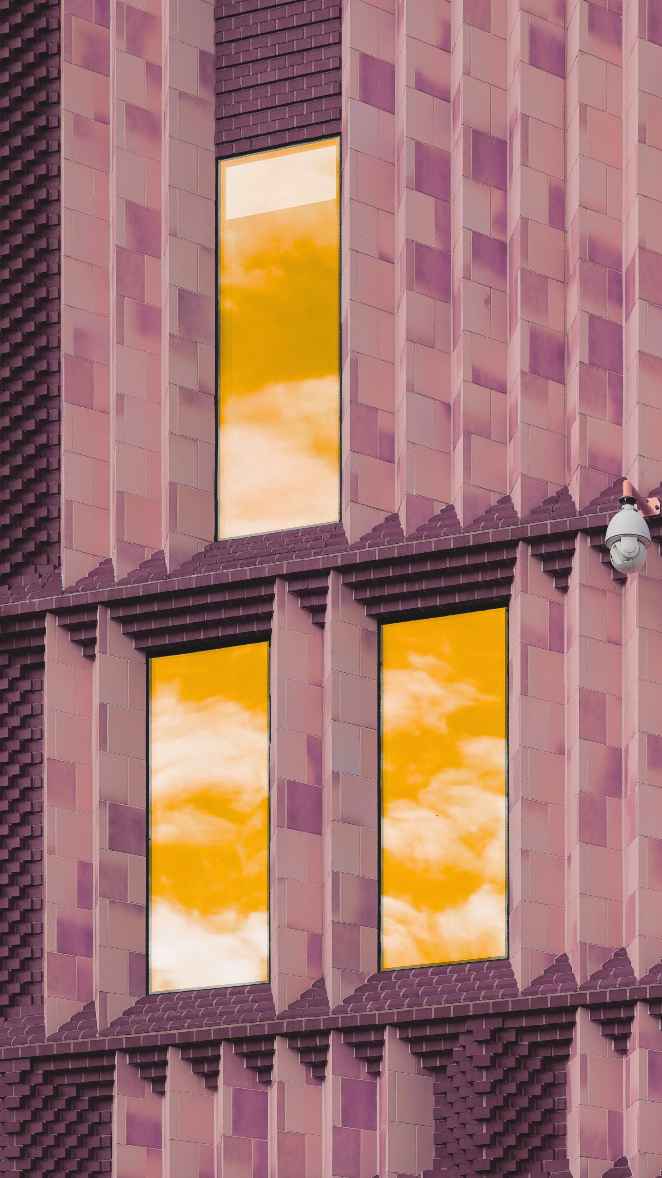 Reflection of a cloudy sky in yellow-tinted windows of a purple building.