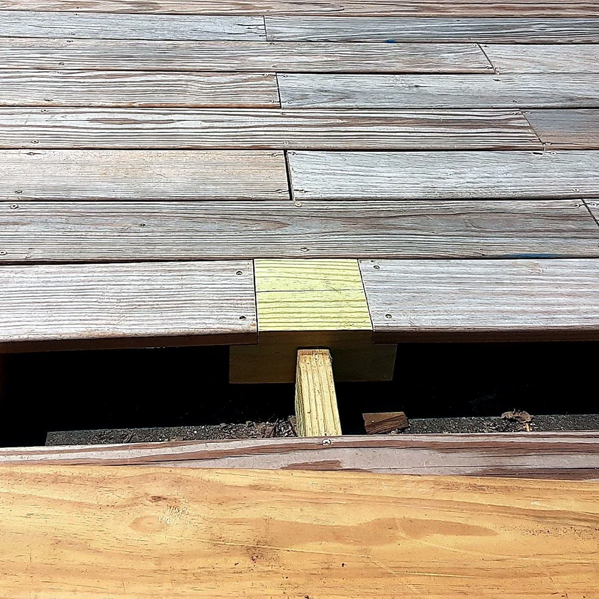 Close-up of a wooden deck with a yellow-painted board and a supporting beam underneath.