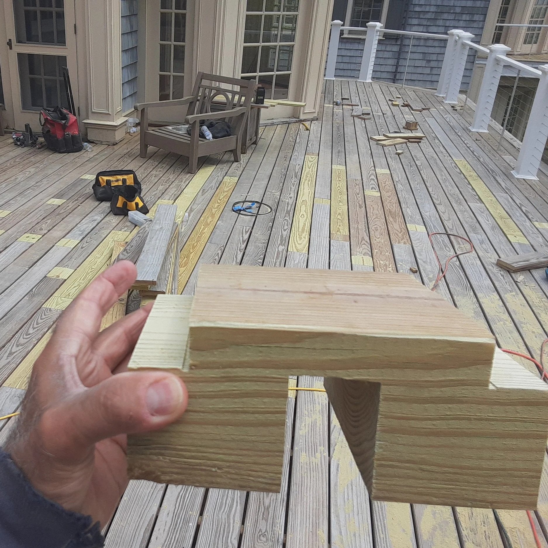 Person holding a piece of wood on a construction deck with tools and other wood pieces scattered around.