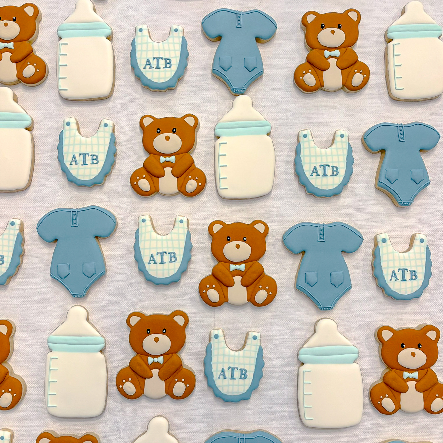 Custom decorative cookies shaped like teddy bears, baby bottles, baby onesies, and bibs, for a baby shower celebration.