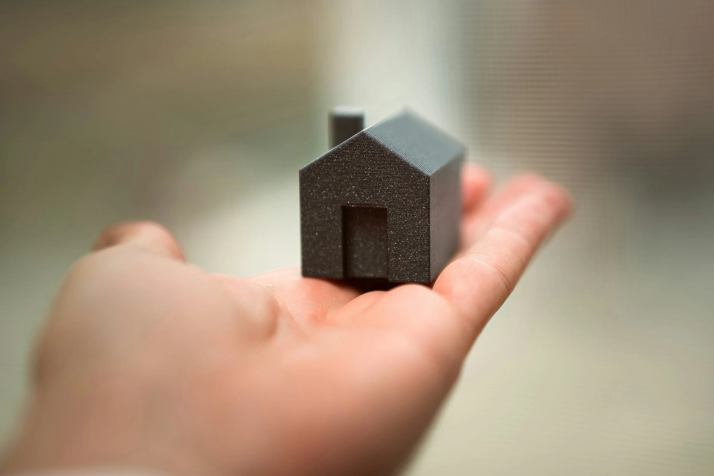 Small black house-shaped object made of foam or similar material, held in a person's hand.